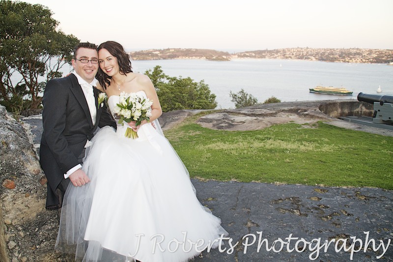 Couple sitting with manly ferry and sydney harbour behind - wedding photography sydney